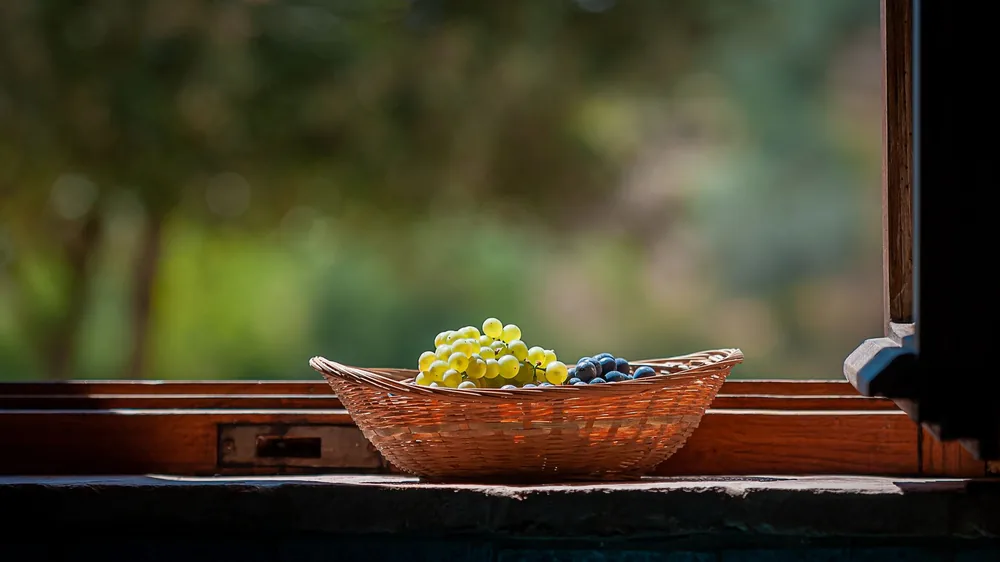 A basket of fresh grapes sits on a windowsill, capturing natural light and colors