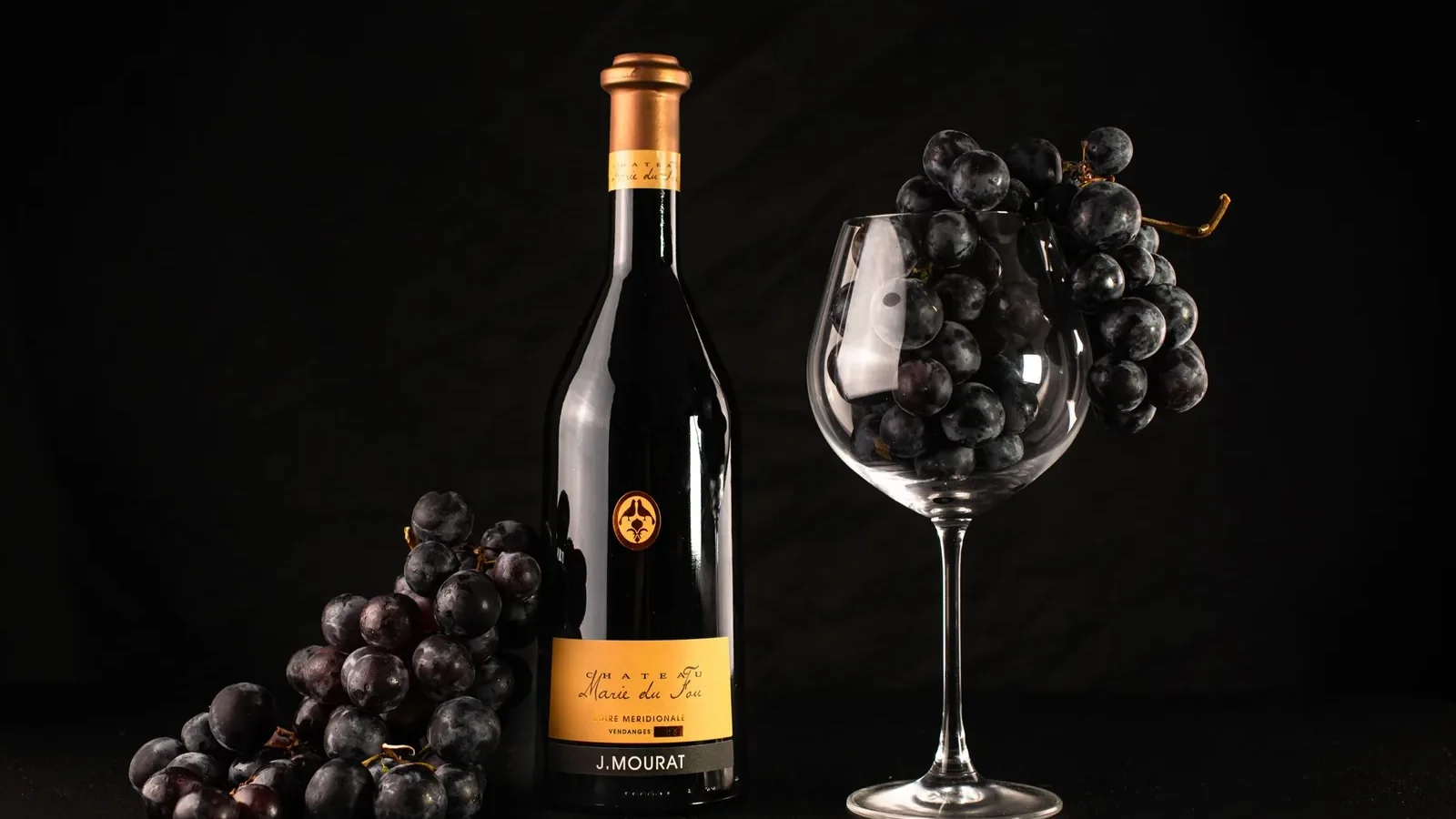 A bottle of red wine with grapes and an empty glass captures elegance and sophistication