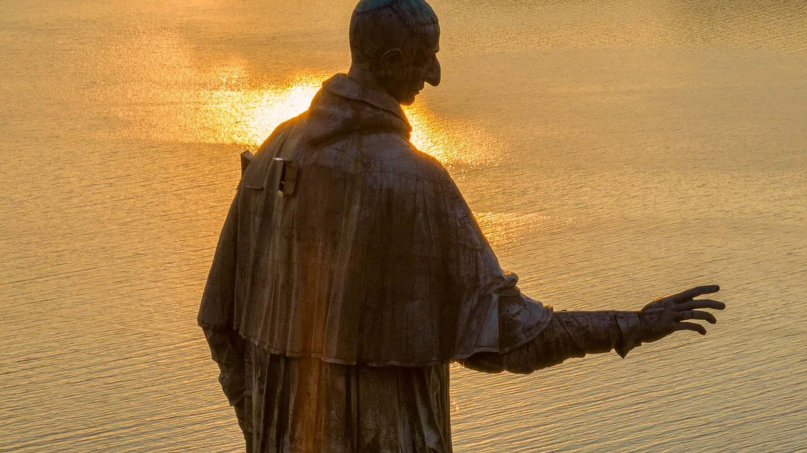A bronze statue gracefully extends over a shimmering lake during golden sunset