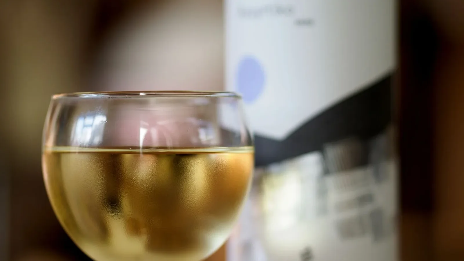 A chilled glass of white wine with an abstract bottle label in the background