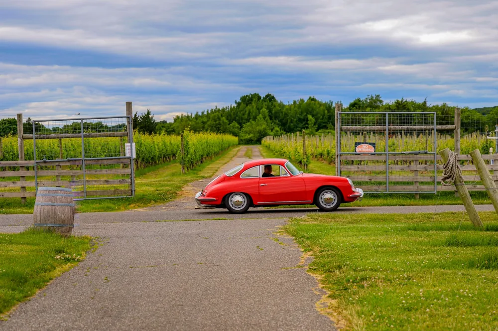 A classic red car parked by a verdant vineyard under a cloudy sky