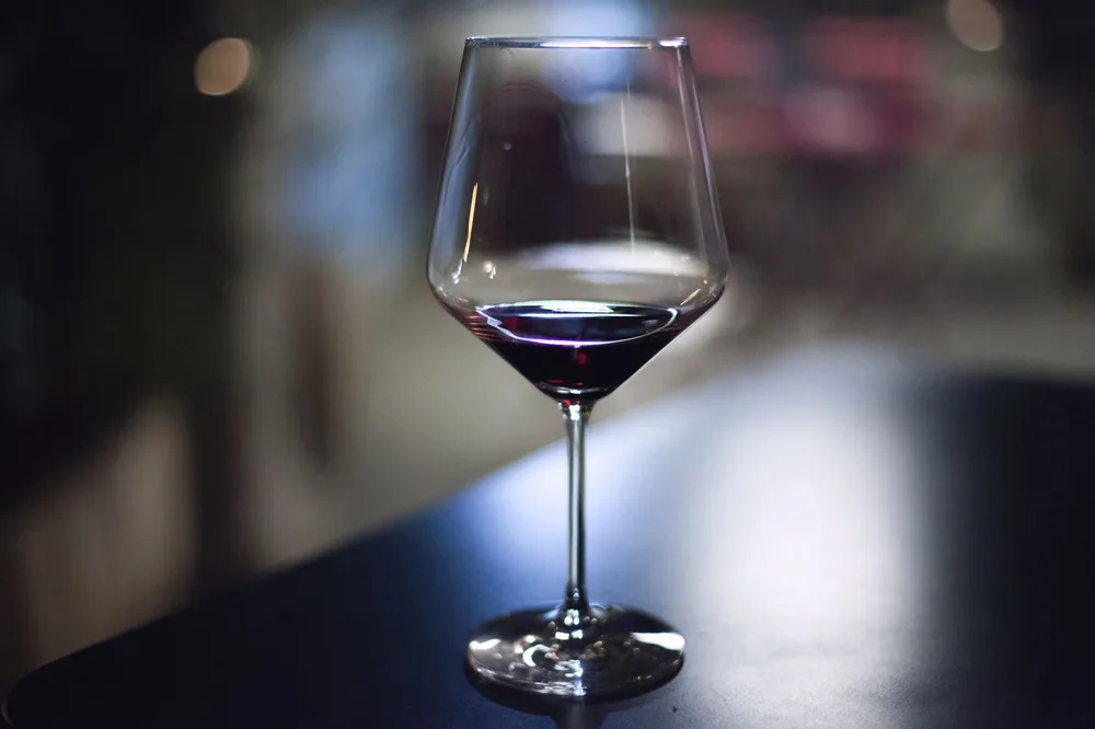 A close-up of a wine glass filled with red wine on a dark table in an indoor setting