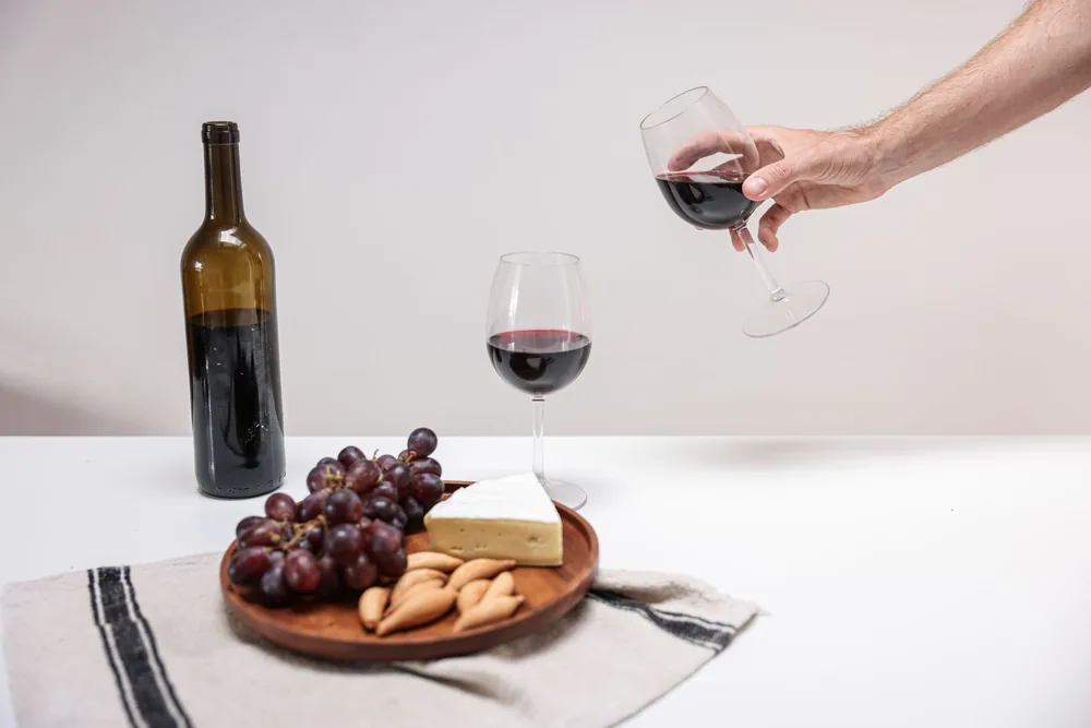 A close-up view of red wine, cheese, and grapes on a stylish charcuterie board