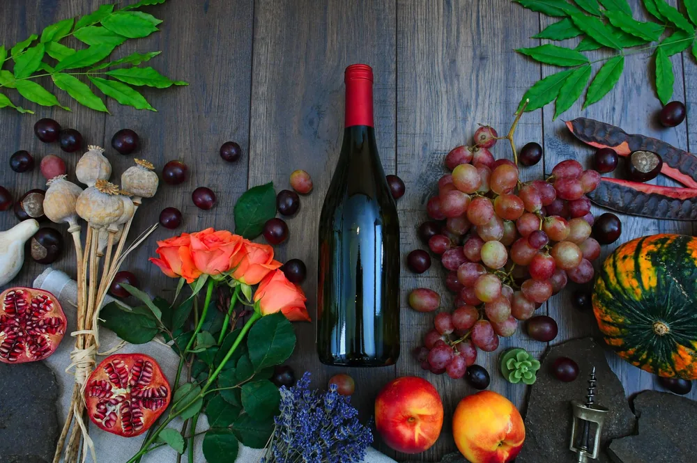 A colorful display of autumn harvest with wine, fruits, and florals on a wooden table