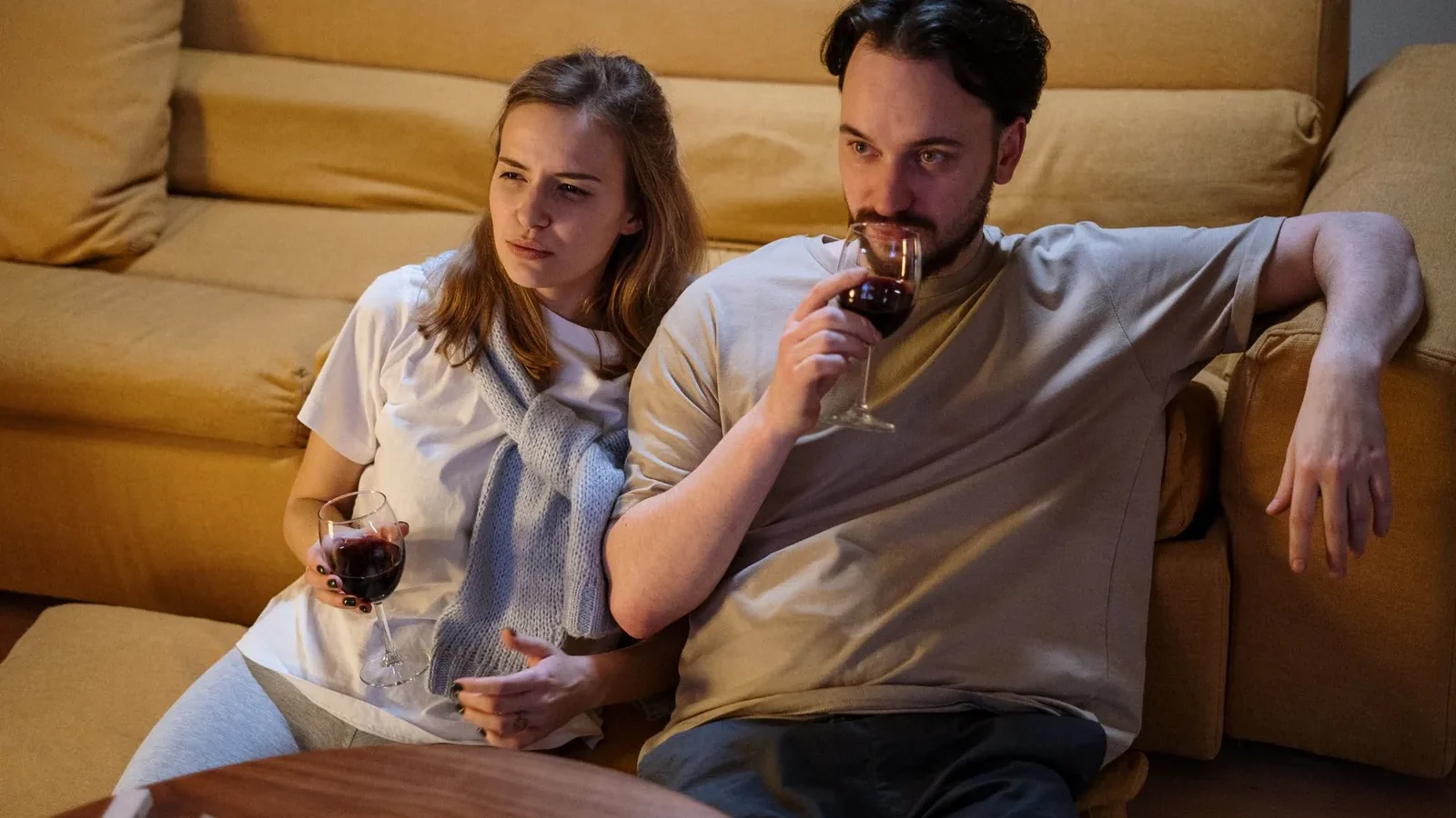 A couple sitting on a sofa at home, enjoying glasses of wine in a cozy setting