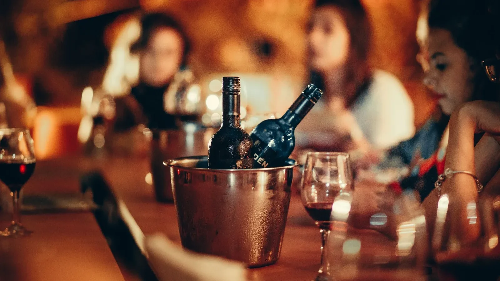 A cozy gathering with wine bottles and glasses on a bar counter, evoking a nightlife atmosphere