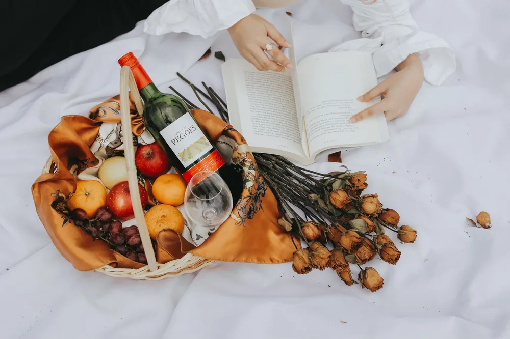 A cozy outdoor picnic featuring wine, fruit basket, dried flowers, and an open book for a calming retreat