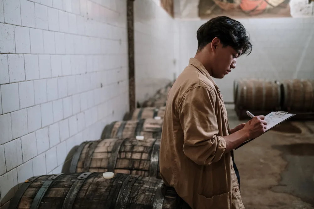 A craft beer expert inspects wooden barrels in a brewery's storage room