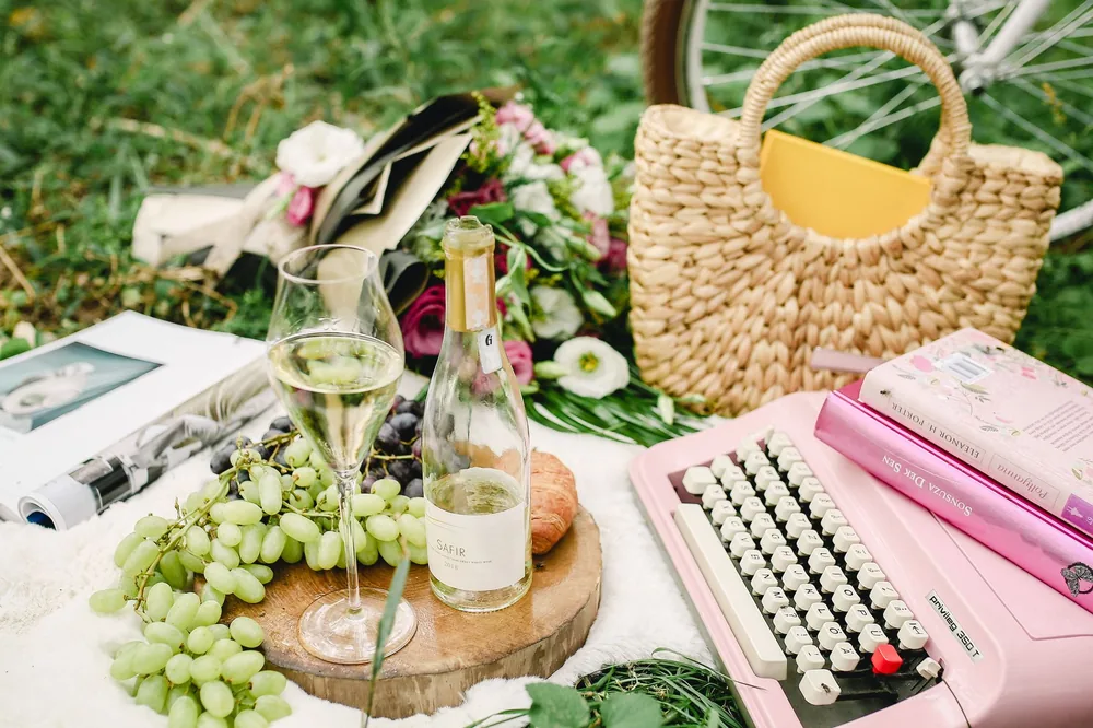 A delightful picnic setup with wine, bouquet, books, and a typewriter on grass