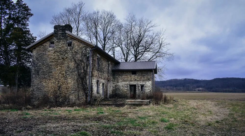 A deserted stone farmhouse in a vast rural field under a cloudy sky, showcasing nature's quiet beauty