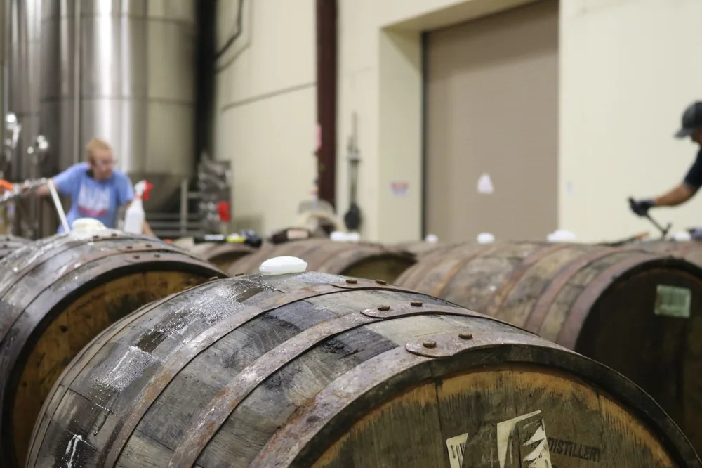 A distillery interior featuring wooden barrels. Workers are busy in the background, showcasing the production process
