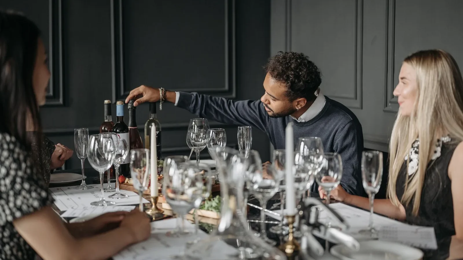 A diverse group of adults enjoying a dinner party indoors with wine and candles