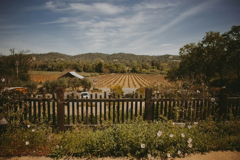 A farm field with a fence and a farm in the background
