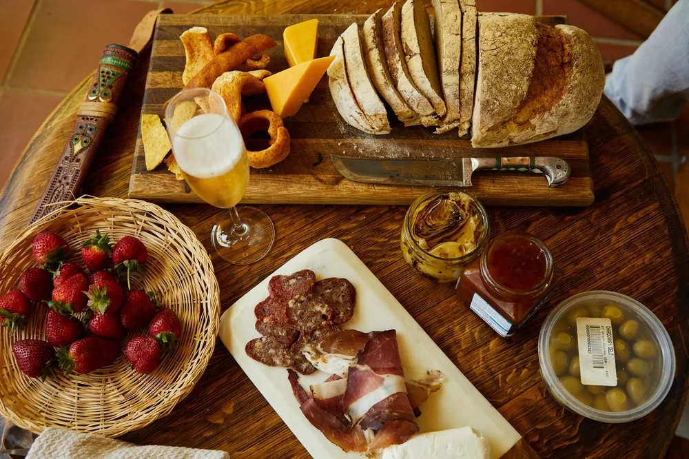 A gourmet charcuterie board featuring sliced bread, meats, cheese, and wine on a rustic wooden table