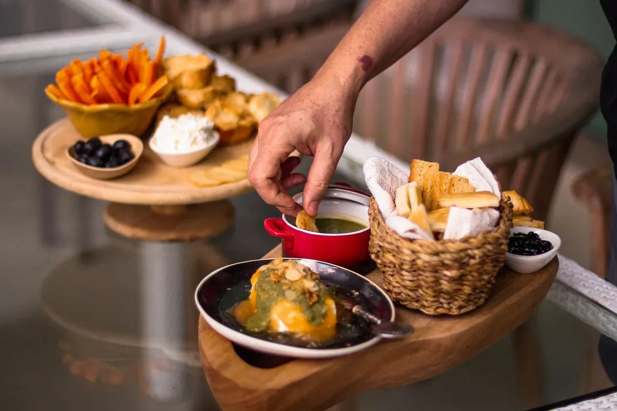 A gourmet platter featuring various breads, cheeses, and a dip with a hand reaching for a piece