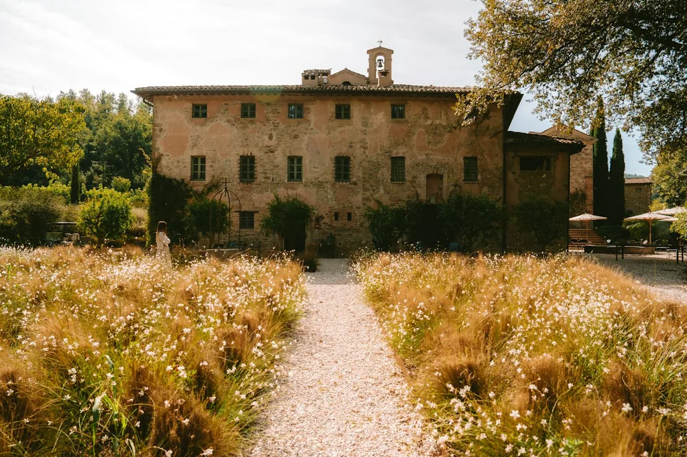 A gravel path through a field of wildflowers leading to a stone villa