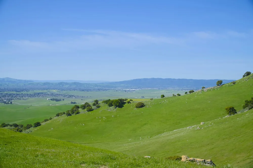A green hillside with blue sky and distant mountains