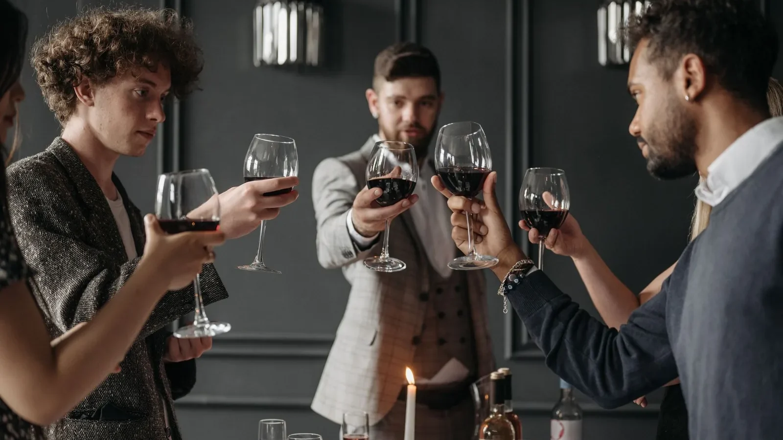 A group of elegantly dressed adults in suits toasting with red wine at a sophisticated party