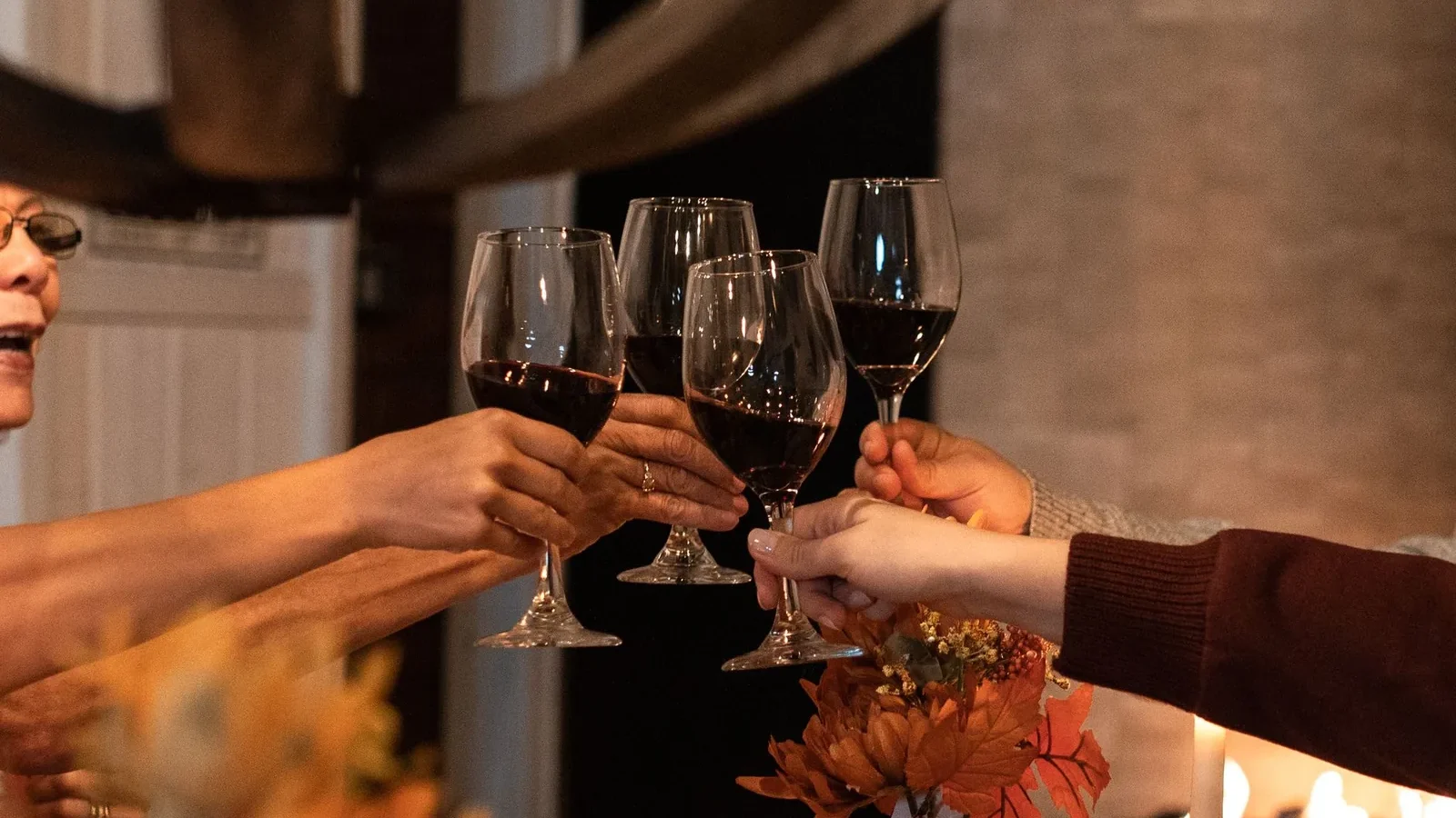 A group of people toasting with red wine glasses, celebrating indoors in a warm, cozy atmosphere