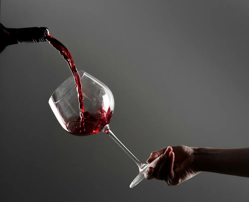 A hand holding a wine glass with red wine being poured into it