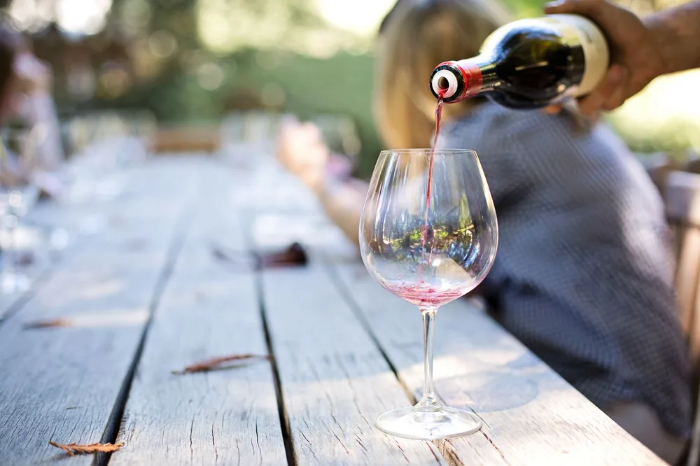 A hand pouring red wine into a glass on an outdoor table, creating a relaxed atmosphere