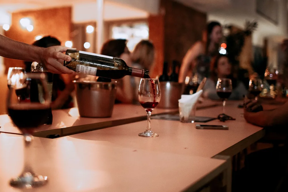 A hand pouring red wine into glasses at an intimate gathering, creating a warm and inviting atmosphere
