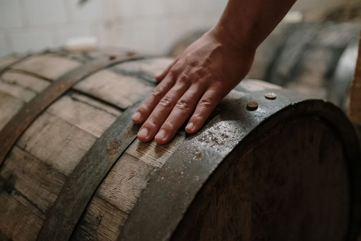 A hand resting on a rustic wooden barrel in a brewing environment