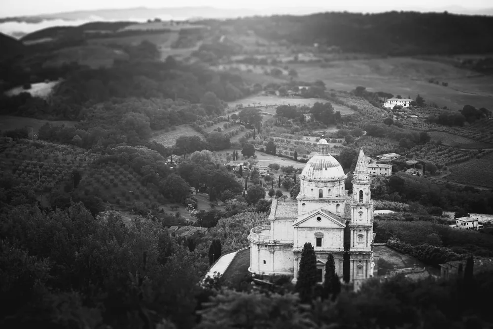 A historic church surrounded by Tuscan countryside, captured in monochrome