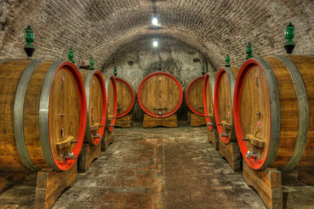 A historic wine cellar with large oak barrels and brick arches, softly illuminated