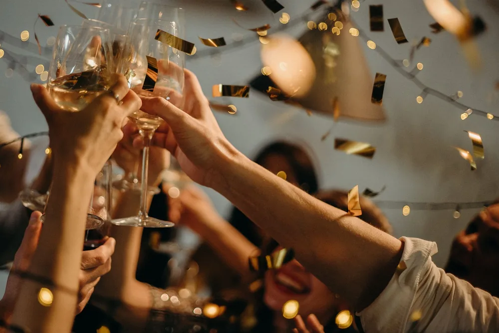 A lively indoor party scene with people toasting champagne glasses amid confetti and warm lights