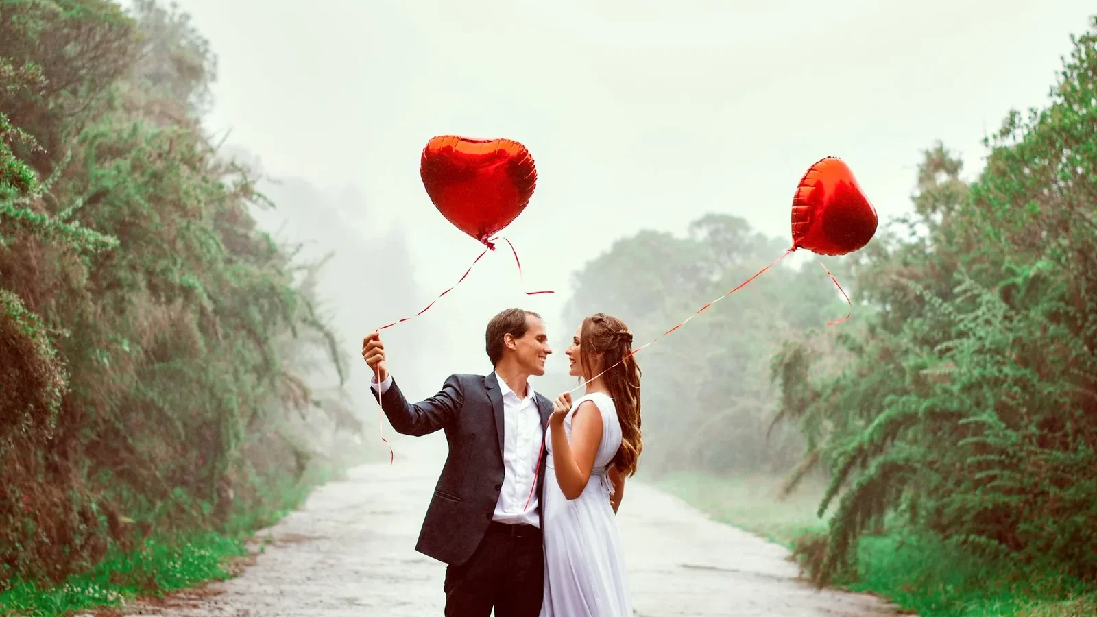 A loving couple embraces with heart-shaped balloons in a foggy park setting