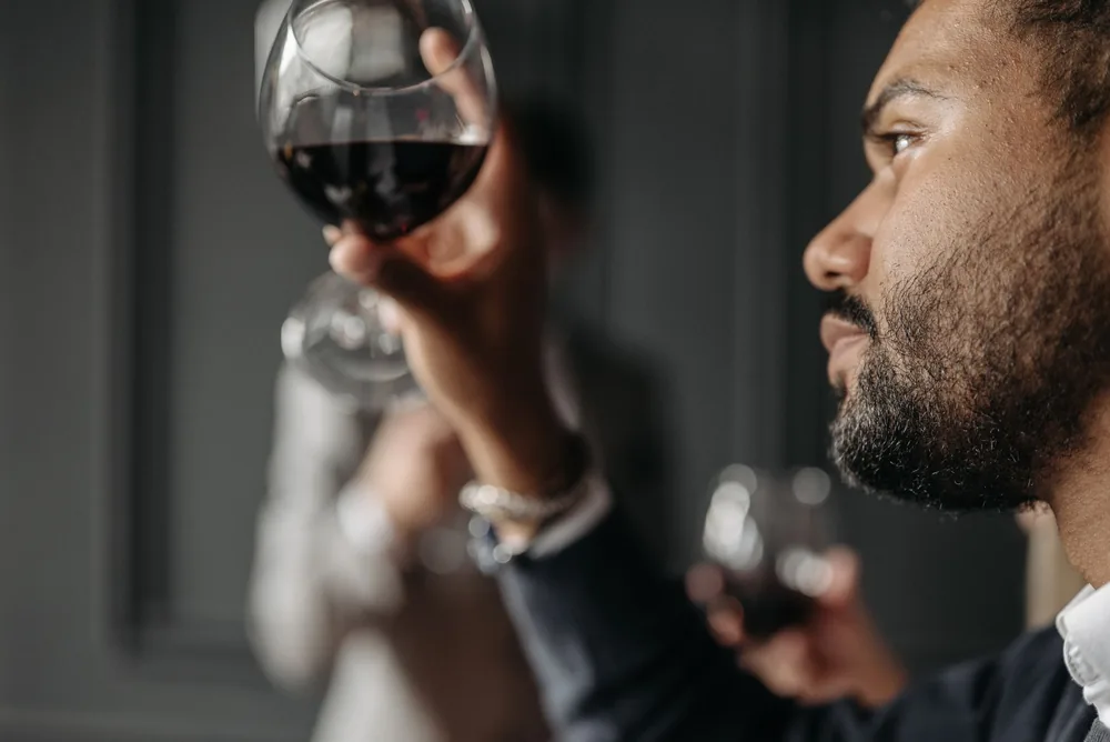 A man admiring a glass of red wine indoors, showcasing a moment of elegance