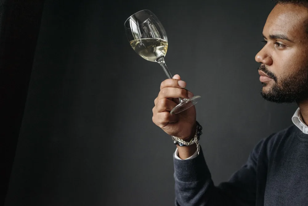 A man carefully examines a glass of white wine in a sophisticated atmosphere