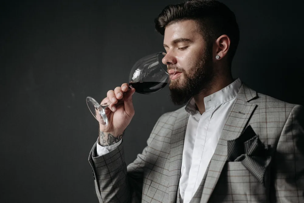 A man in a plaid suit savoring red wine against a gray background