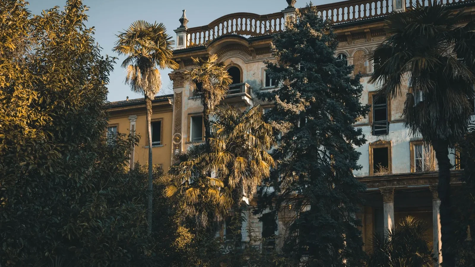 A mysterious abandoned villa surrounded by lush trees in a warm sunset light