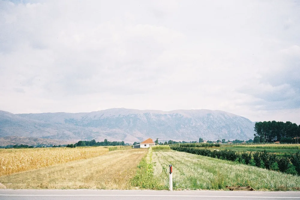 A peaceful rural scene with fields and a small farmhouse under a cloudy sky
