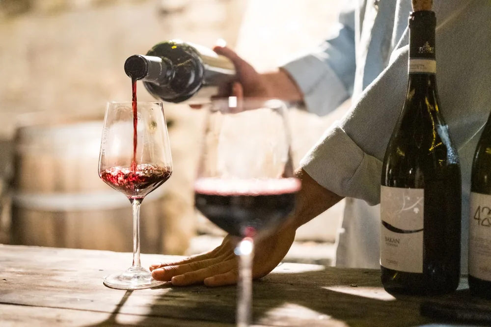 A person pouring red wine into a glass in a rustic, cozy wine bar setting