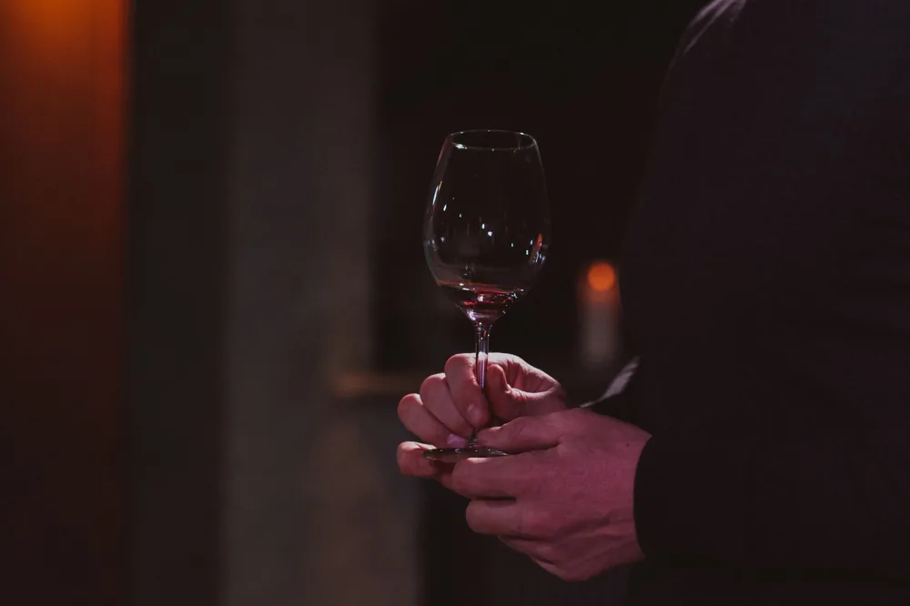 A person's hands holding a glass of red wine in a dimly lit indoor setting