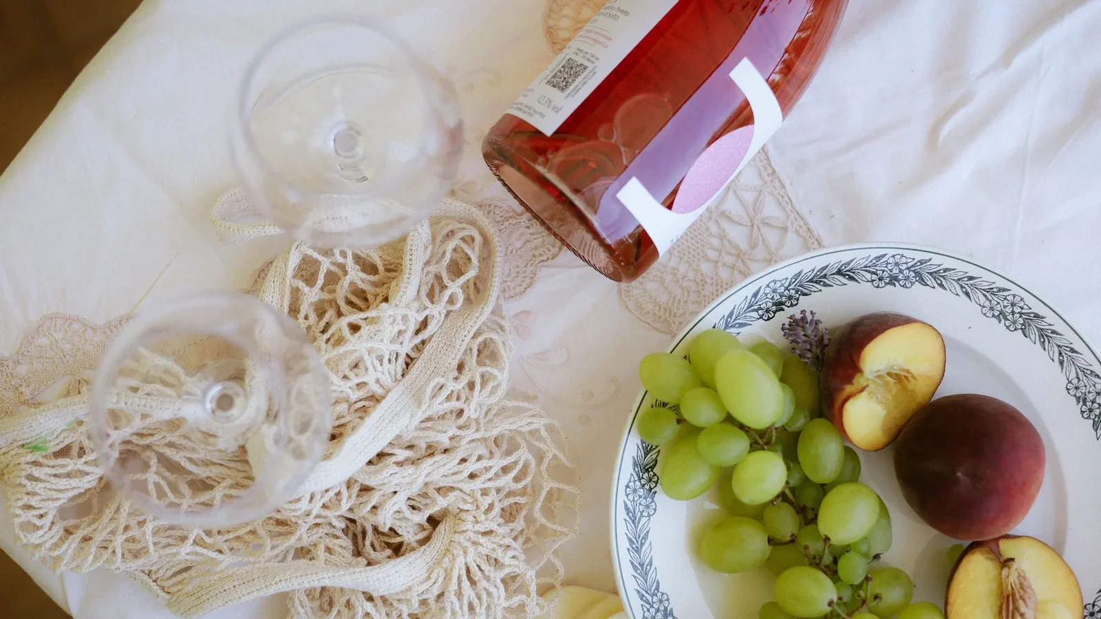 A refined picnic scene featuring wine, green grapes, and peaches on a decorative tablecloth