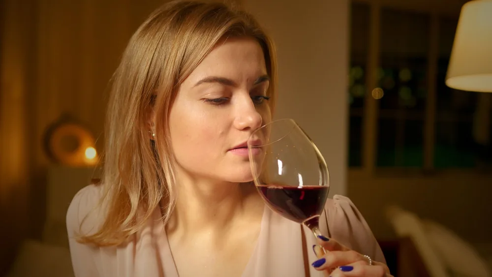 A relaxed woman savors a glass of red wine in a cozy indoor setting
