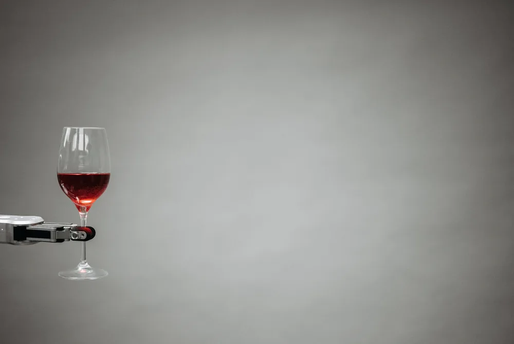 A robotic arm precisely holding a glass of red wine against a neutral background