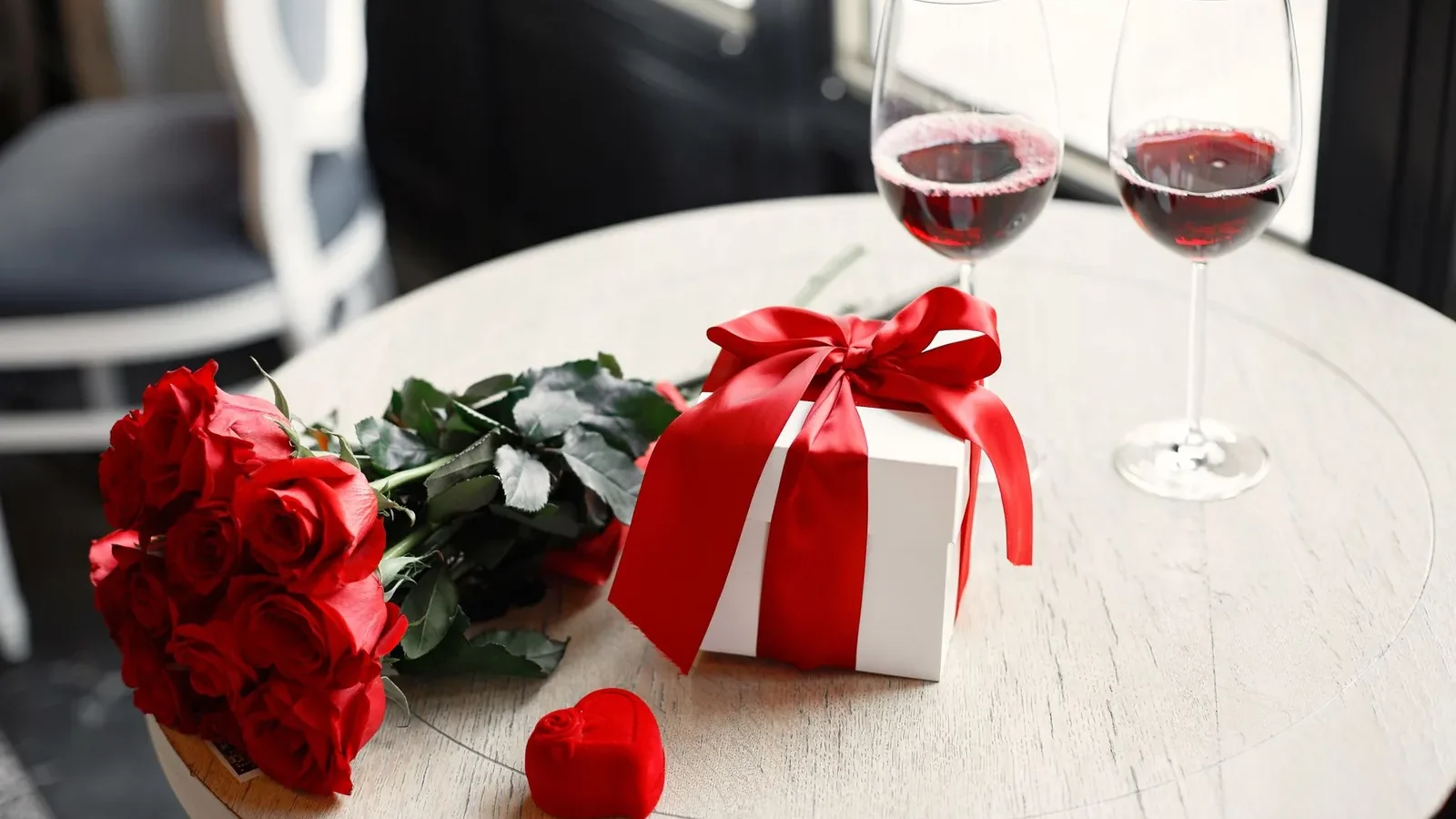 A romantic table setting with red roses, gift box, and red wine glasses, perfect for Valentine's Day celebration