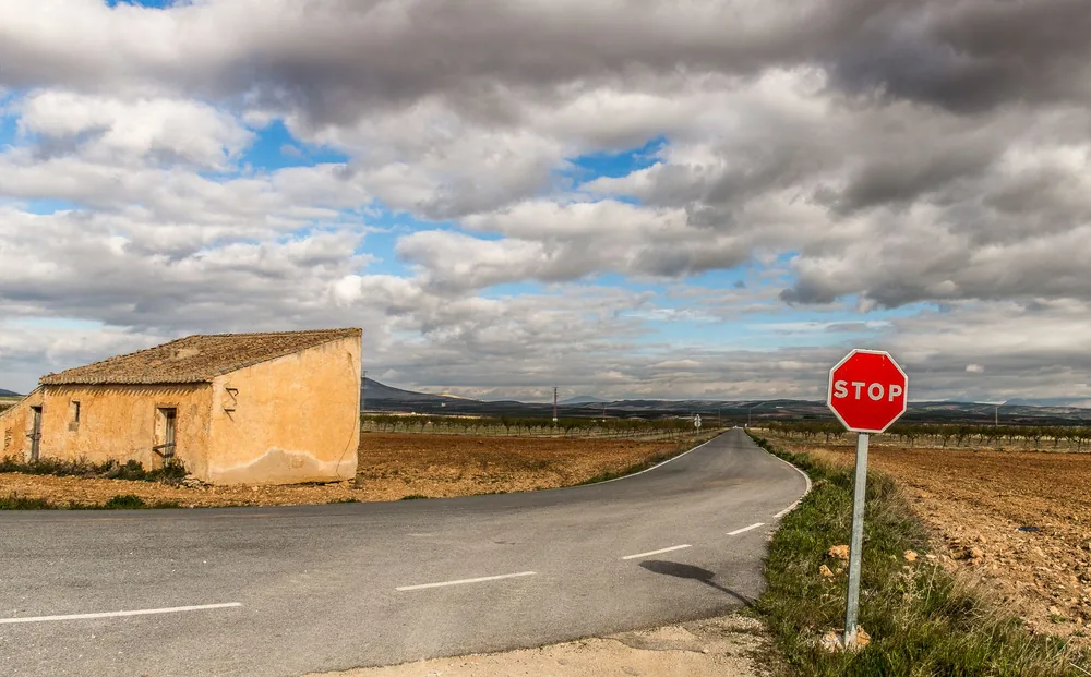 A rural landscape featuring a road, a stop sign, and a small building under cloudy skies