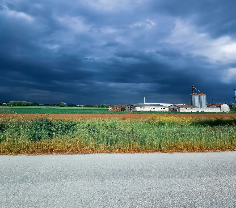 A rural landscape featuring fields and farm buildings under an overcast sky