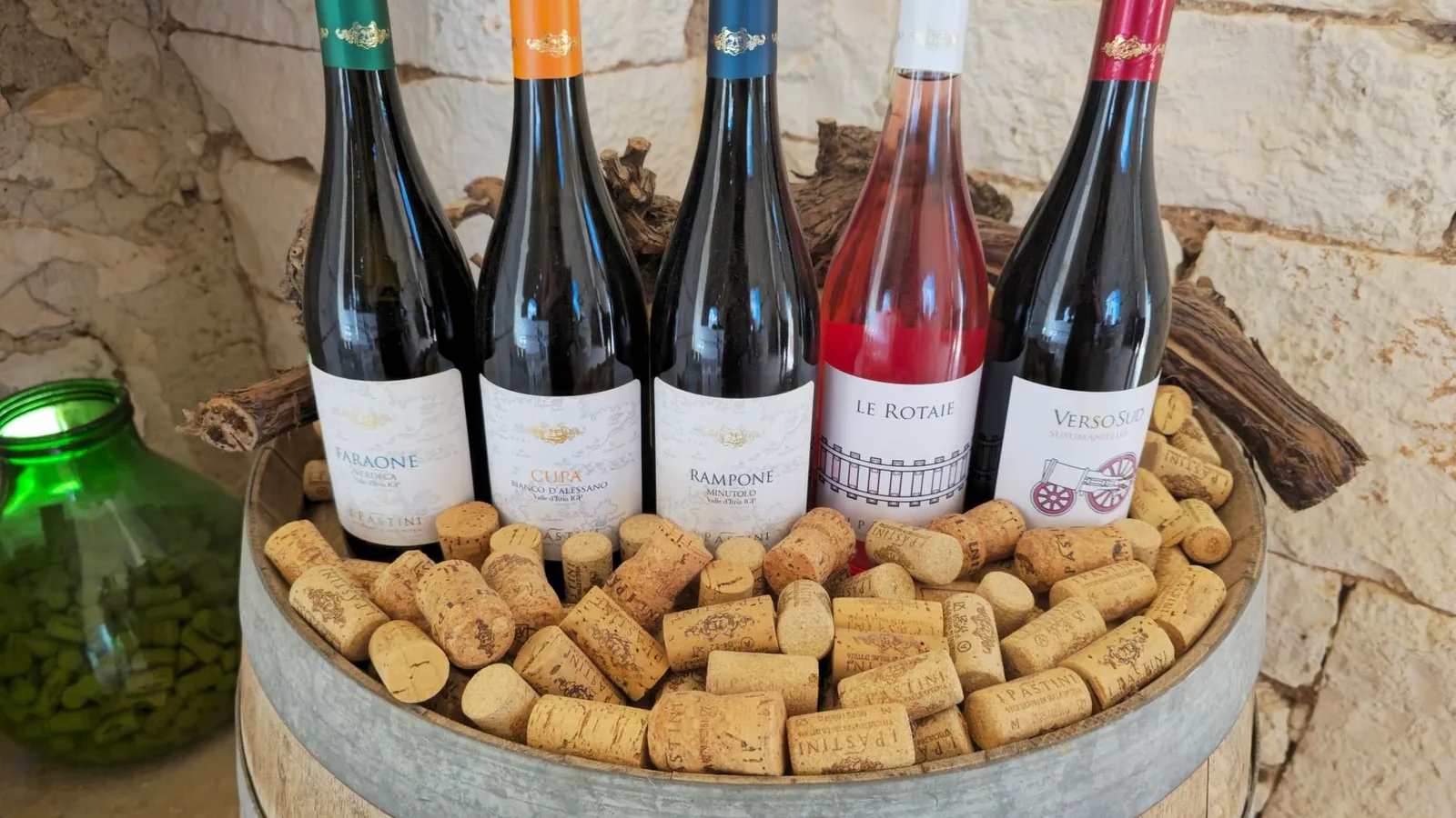 A rustic display of diverse wine bottles and corks on a barrel with a stone wall background