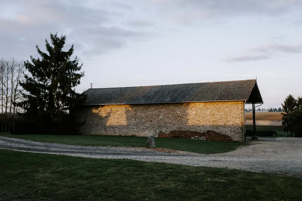 A rustic farm barn stands amidst a serene rural landscape during sunset with gravel path and trees