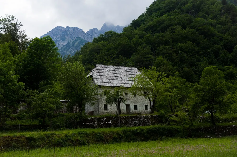 A rustic farmhouse nestled amidst lush green mountains and trees, perfect for travel and nature themes