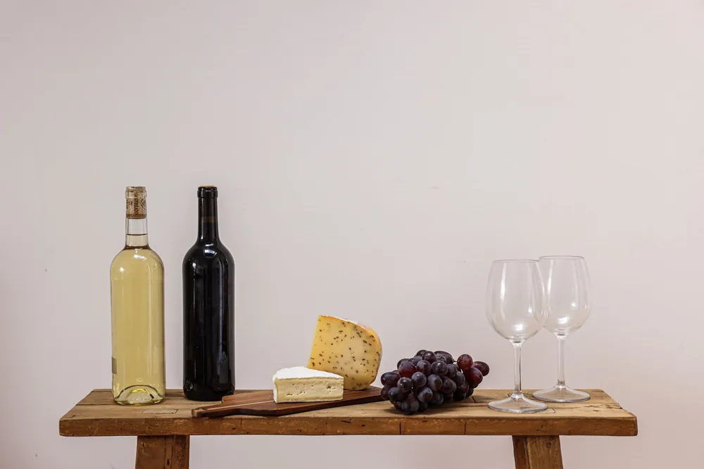 A rustic setting with wine, cheese, grapes, and wine glasses on a wooden table