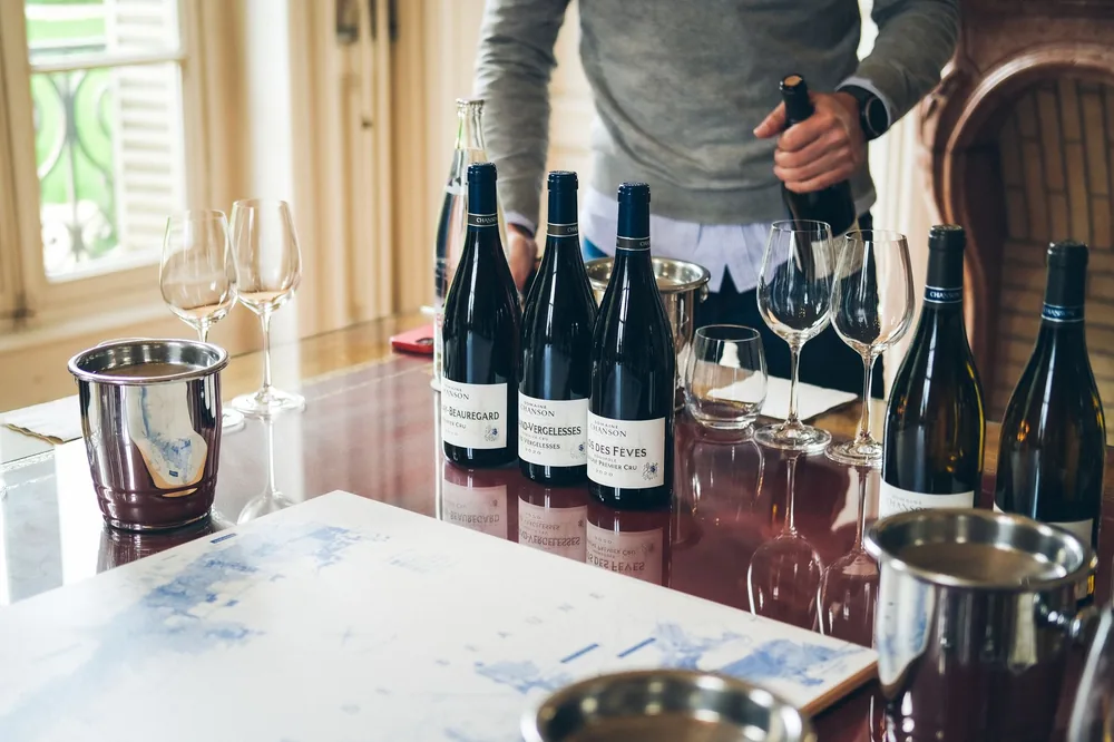 A sommelier pouring wine from bottles on a restaurant table with glasses and buckets