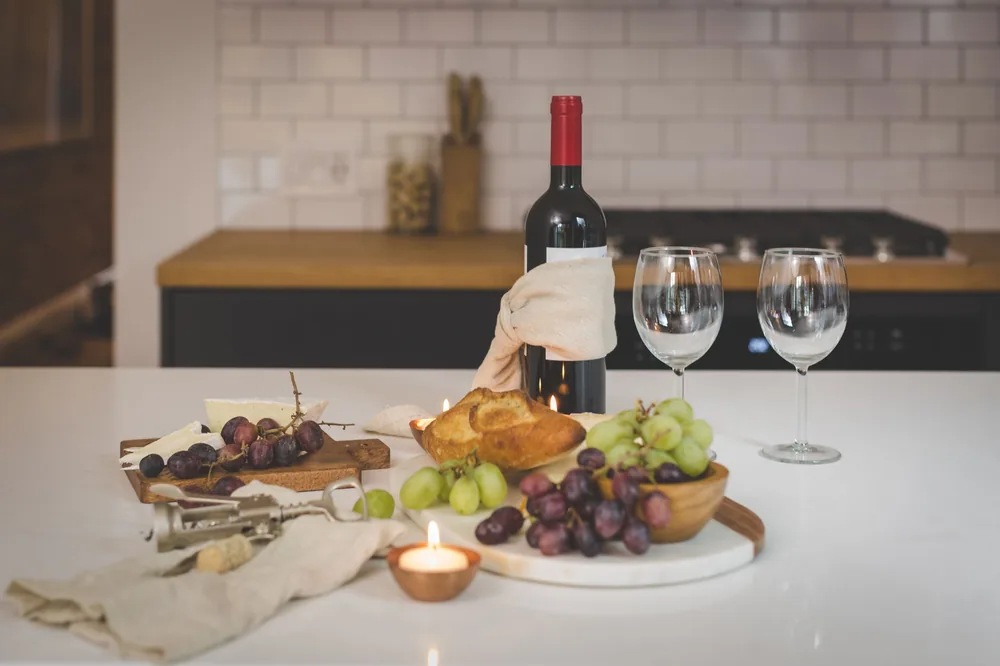 A sophisticated indoor setting featuring red wine, cheese, grapes, bread, and candlelight